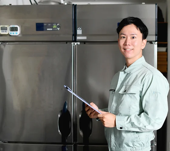 Smiling technician standing in front of commercial refrigerators, representing commercial refrigerator repair services in Sellersburg, IN.