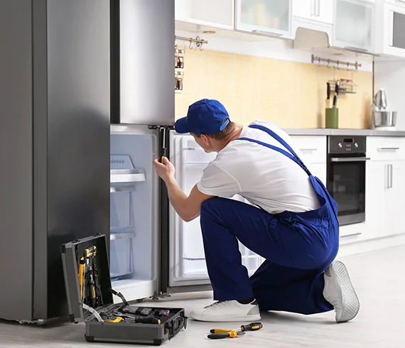 Technician repairing a residential refrigerator in a kitchen, illustrating residential refrigerator repair services in Jeffersonville, IN.