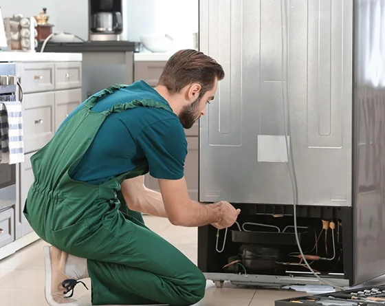 Technician repairing a refrigerator in a kitchen, highlighting same-day refrigerator repair services in New Albany, IN.